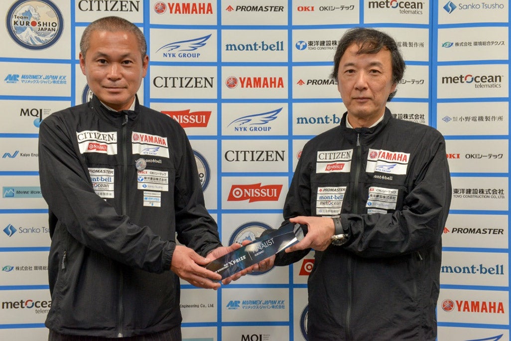 img src="/s3assets/articles/1b57910c41c7f325ccb9ea9205a44dd4.jpg" alt="「Round2実海域競技」への進出を果たした「記念盾」を手に決意を新たにするKDDI総合研究所の西谷明彦と小島淳一