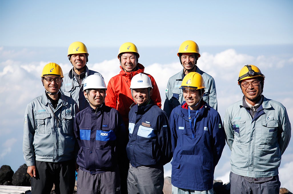今回の富士山プロジェクトチームの面々。「富士山の電波対策はチームワークが大切。チーム内に良い雰囲気をつくることも私の大事な仕事のひとつです」と、プロジェクトの中心人物である松原（前列中央）は語る。彼らが手を尽くしているからこそ、山頂でもスマートフォンや携帯電話を使うことができるのだ